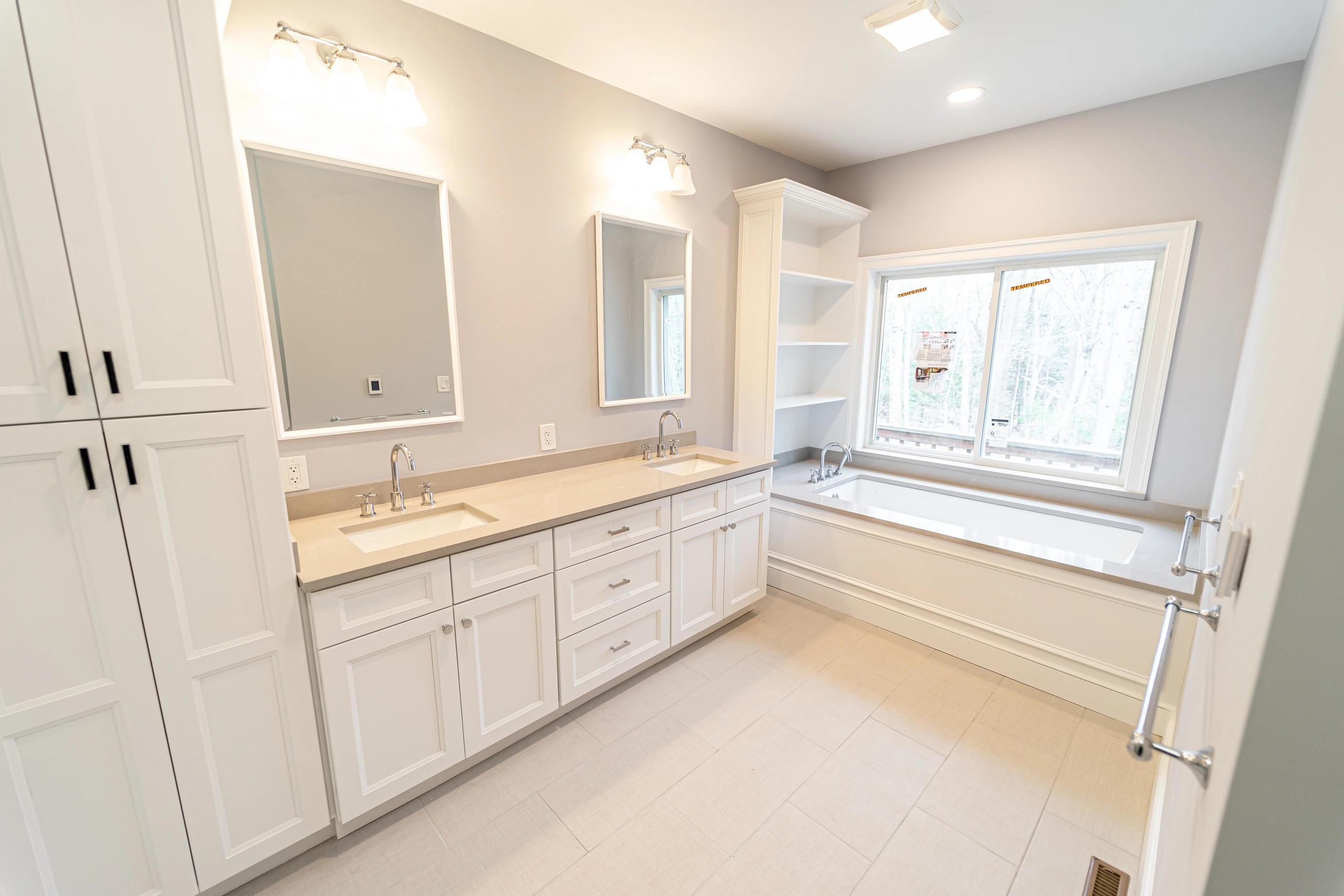 Linen tower, double vanity, and soaking tub in a bright white bathroom remodel in Sherborn, MA