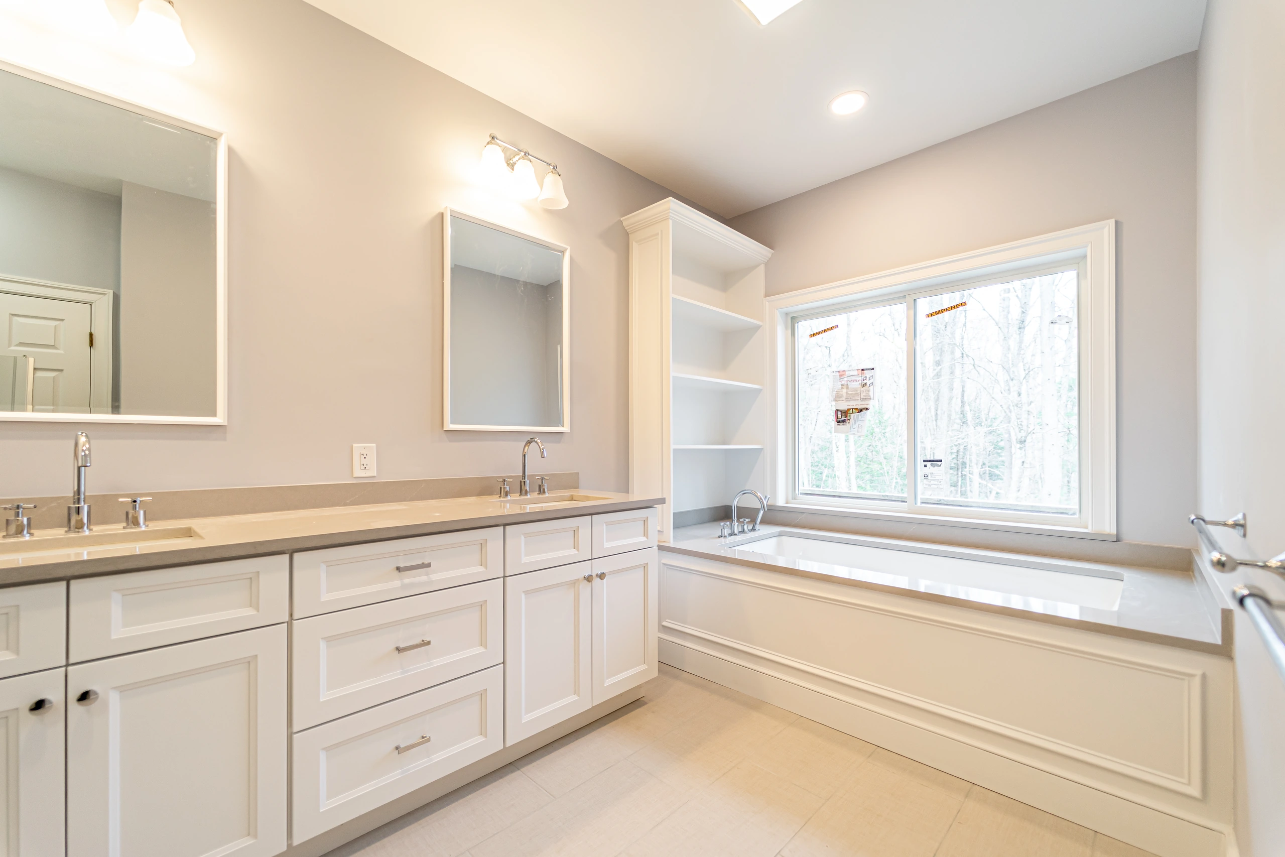 Finished bathroom remodel in Sherborn, MA, with white double vanity and soaking tub under a wide window