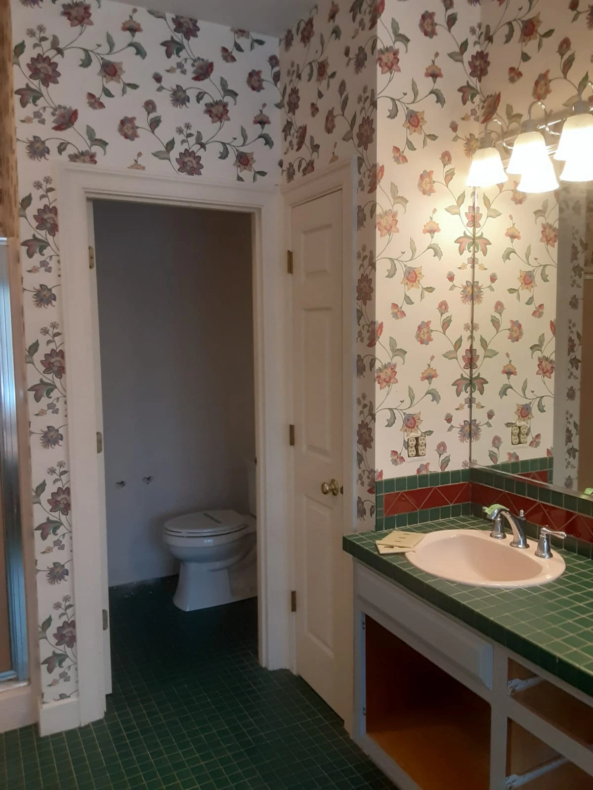 Bathroom before remodel in Sherborn, MA, with green tile vanity, floral wallpaper, and toilet room
