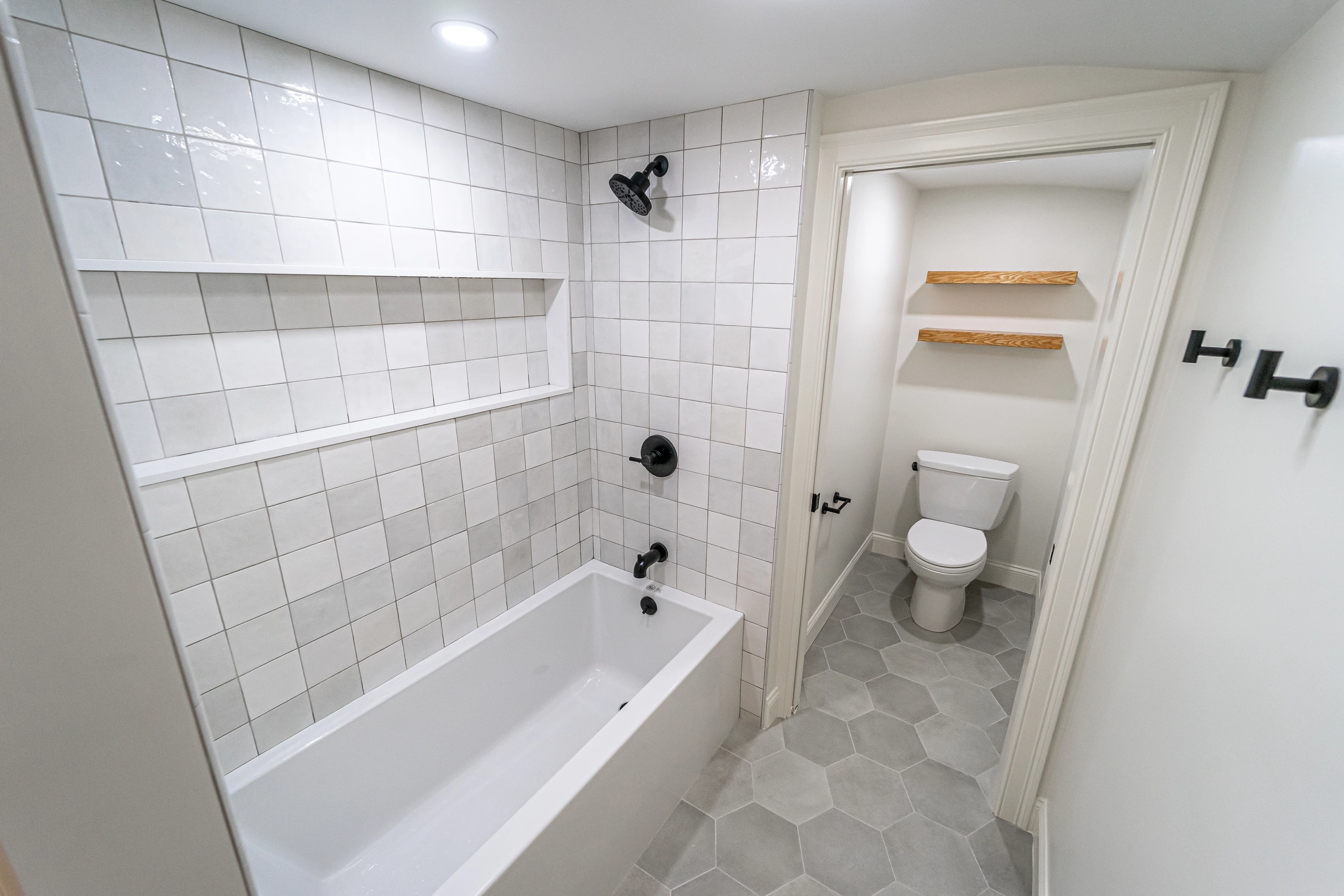 Soaking tub with square tile surround, long niche, and black fixtures, home addition in Natick, MA