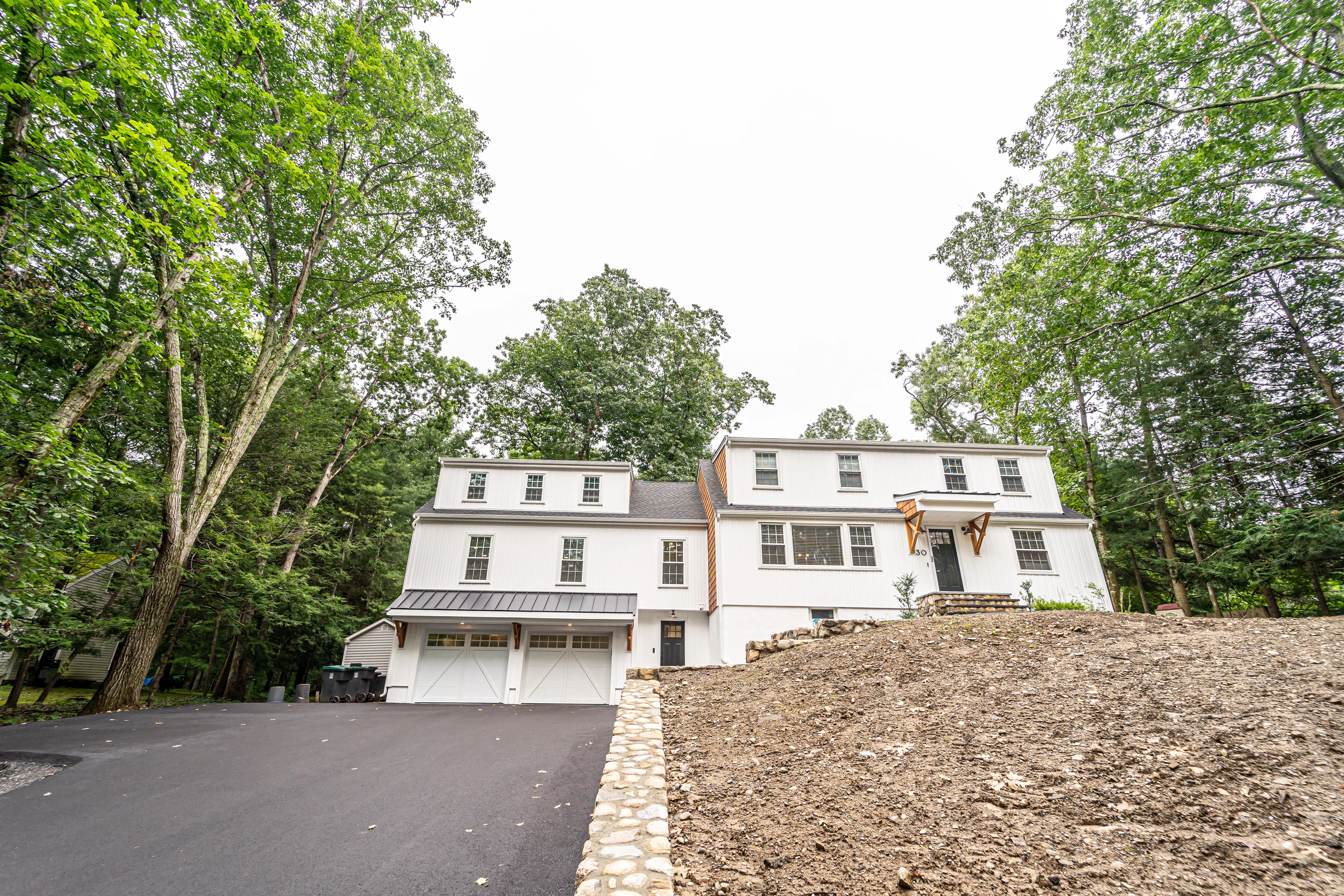 Finished white board and batten home with new garage addition seen from the driveway, home addition in Natick, MA
